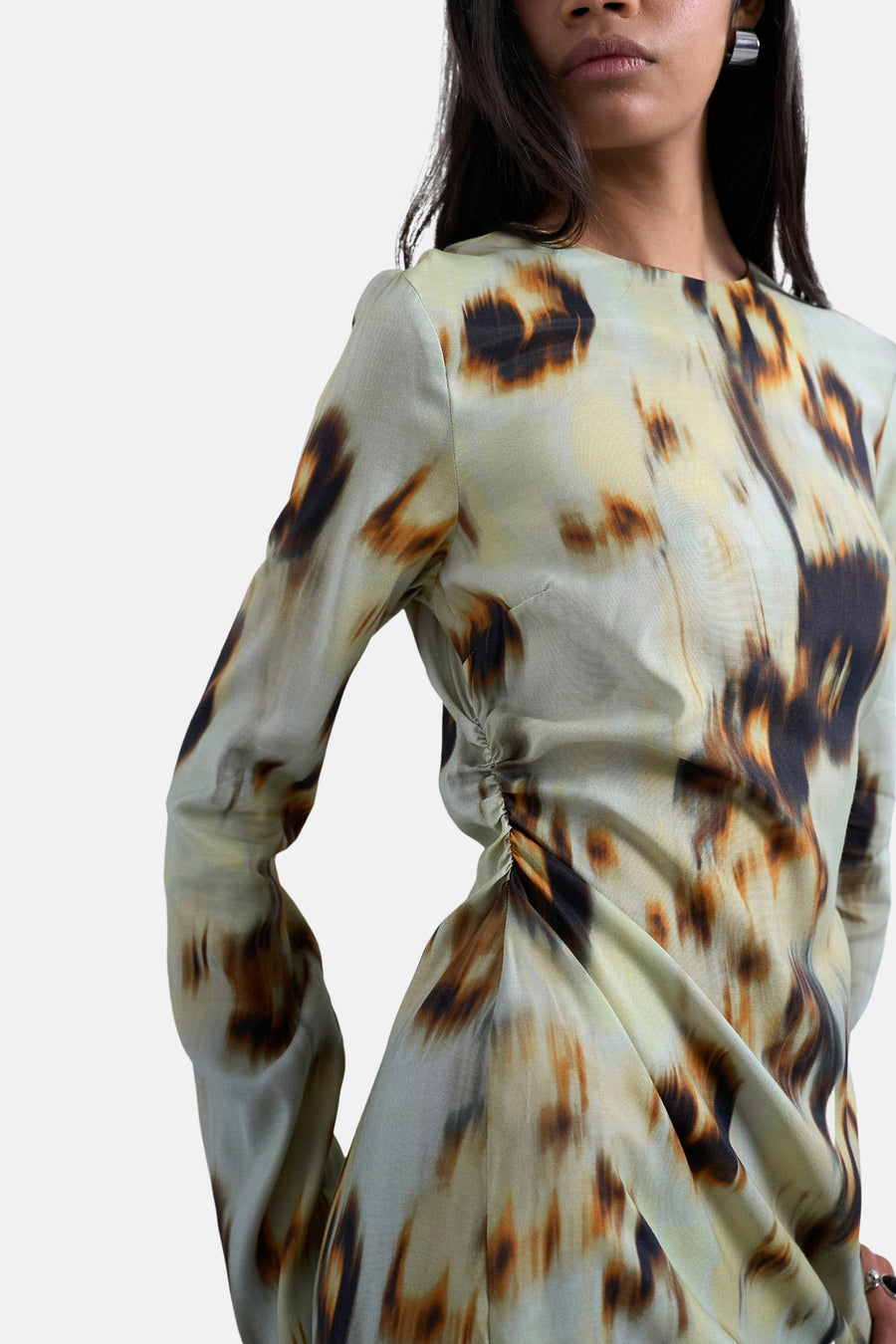 Vrouw met een lange mouw jurk met abstracte print, in een studio gefotografeerd.