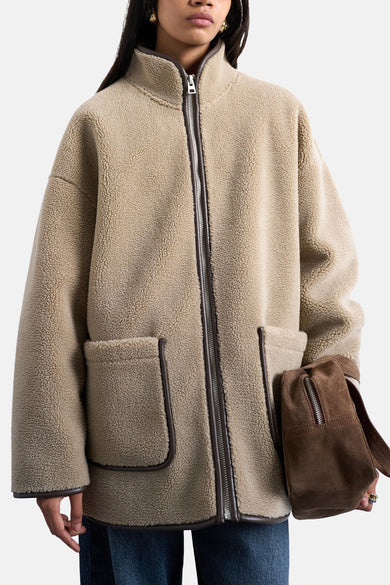 Manteau beige de TOPSHOP, avec fermeture éclair et poches, et une sacoche en cuir de marron.