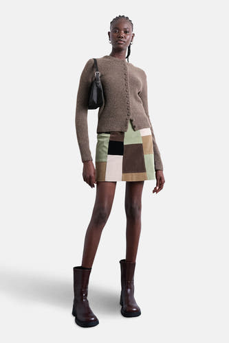 Cardigan marron de TOPSHOP, avec fermeture à boutons et longues manches, associé à une jupe patchwork courte et des bottes marrons.