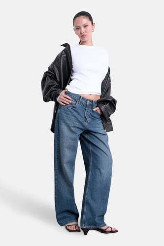 T-shirt blanc à manches longues de TOPSHOP, porté sous une veste en cuir noire et des jeans larges.