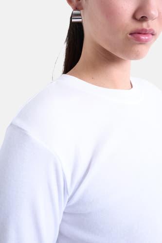T-shirt blanc à manches longues de TOPSHOP, gros plan d'un modèle avec des boucles d'oreilles argentées.
