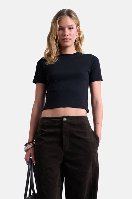 T-shirt noir à manches courtes de TOPSHOP, porté avec un pantalon marron et des bracelets, contre un fond blanc.