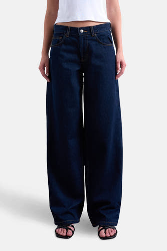 Jean bleu marine droit de TOPSHOP, avec des surpiqures jaunes, associé à un t-shirt blanc et des sandales noires.