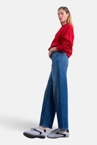 Jeans coupe droite bleu moyen en denim de TOPSHOP, à jambes larges et porté avec un pull rouge.
