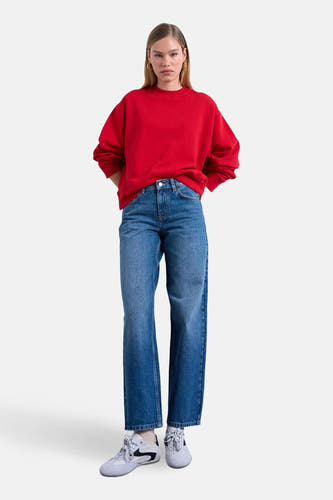 Rechte jeans van midblauw denim van TOPSHOP, gecombineerd met een rode sweater en witte sneakers.