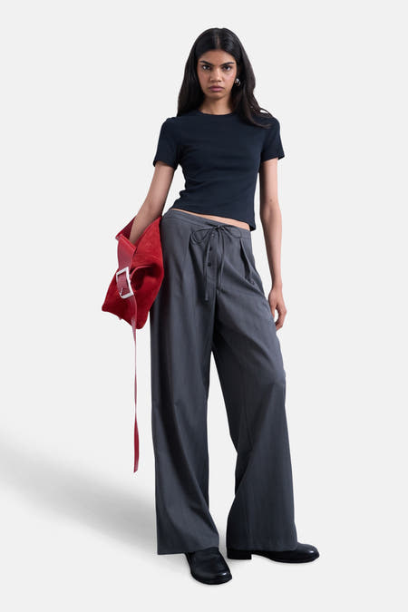 Pantalon gris de TOPSHOP, avec des jambes larges et une fermeture éclair, associé à un t-shirt bleu foncé et une poche main rouge.