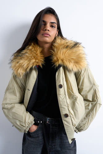 Manteau court vert de TOPSHOP, avec un col en fausse fourrure et une fermeture à boutons, associé à un pull noir et des pantalons en cuir.