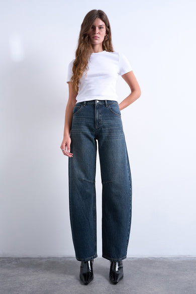 Jean spécial de TOPSHOP en denim bleu et noir, avec des jambes larges et porté avec un T-shirt blanc et des bottines noires.