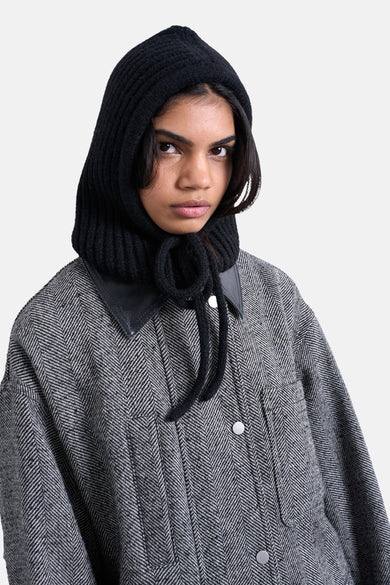 Vrouw met zwarte gebreide kap, grijze jas met visgraatmotief en leren kraag.
