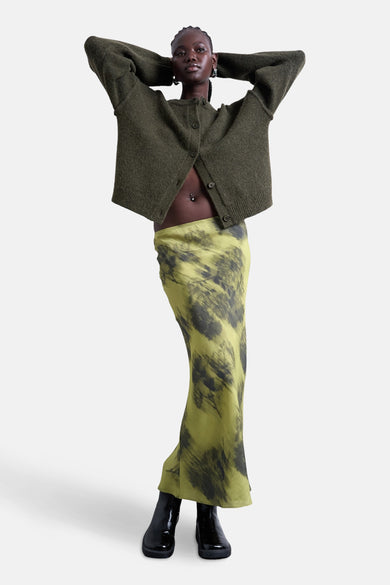 Robe longue verte de TOPSHOP, avec des taches noires abstraites et associée à un cardigan en laine et des bottines noires.