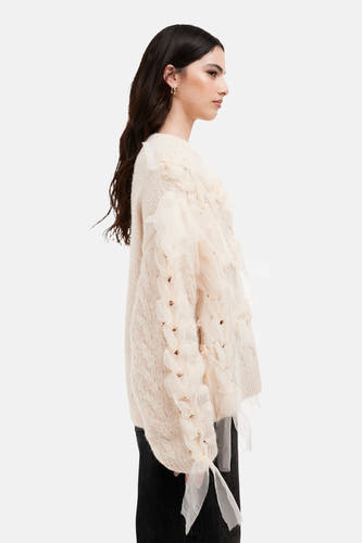 Veste écru ronde encolée de TOPSHOP, avec motif côtelé et bandes d'organza décoratives, vue de côté, associée à un jean noir et des boucles d'oreilles dorées.