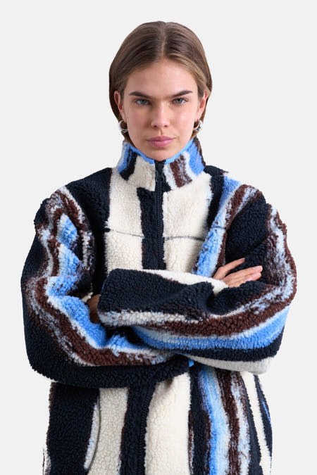 Manteau court multicolore de TOPSHOP, avec des rayures verticales et une texture teddy, porté avec un pull marron et des jeans bleus.