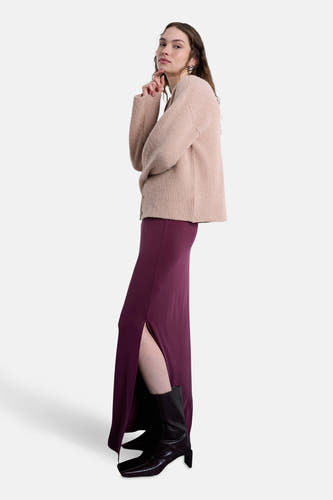 Longue robe rouge de TOPSHOP, avec une fente sur le côté, associée à des bottes noires et un gilet beige.