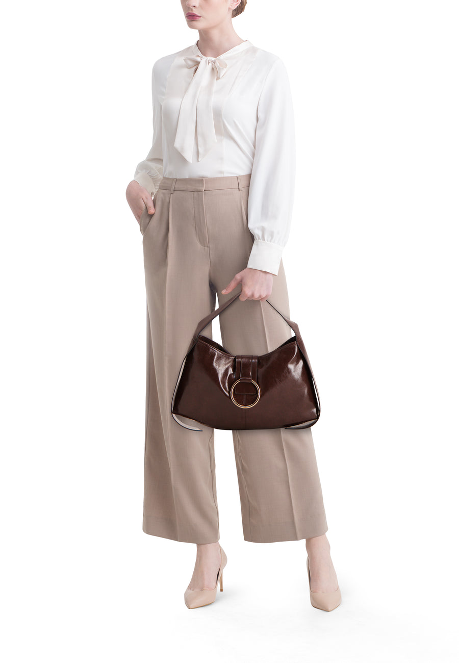 Vrouw in beige broek en bloes met bruine handtas en beige hakken.
