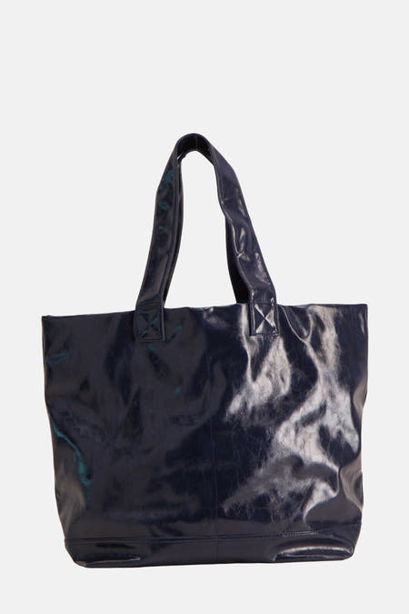 Sac à main bleu de TOPSHOP, avec une texture brillante, porté avec une blouse blanche et un pantalon beige et des talons.