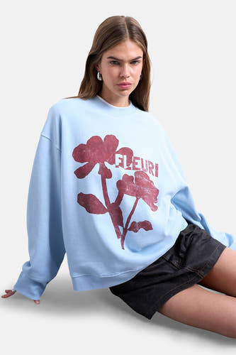 Pull-over bleu de TOPSHOP, avec un imprimé de fleurs rouges et le texte 'FLEURI', porté avec une jupe noire.