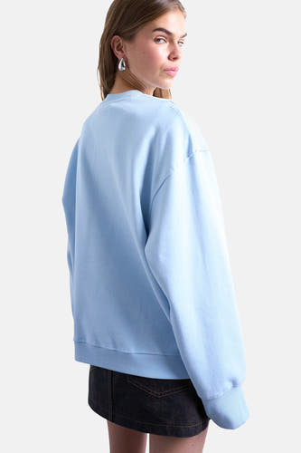 Pull-over bleu de TOPSHOP, avec des manches longues et un col rond, porté avec une jupe bleu marine.