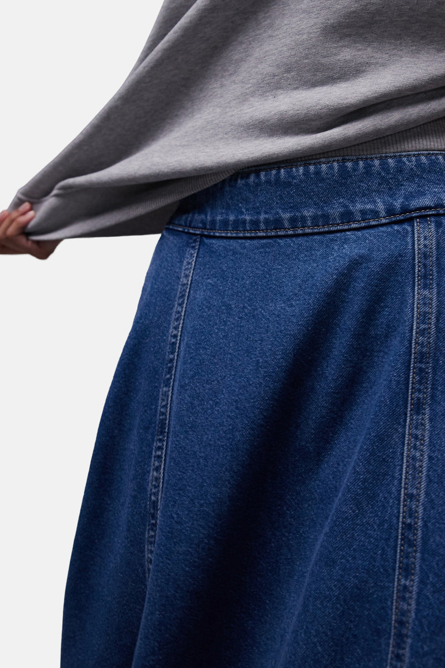 Jupe trapèze en denim bleu moyen TOPSHOP avec coutures verticales, portée par une personne portant un sweat-shirt gris.