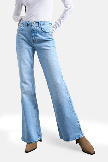Jean évasé en denim bleu clair de TOPSHOP, associé à des bottines marron à talons et une chemise blanche à manches longues.