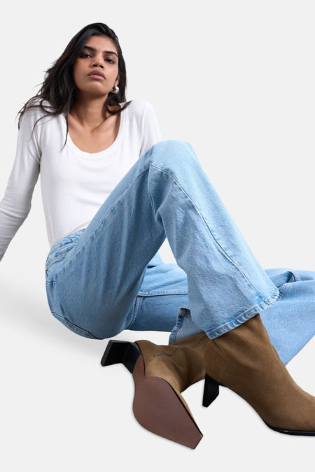 Flared jeans van lichtblauw denim van TOPSHOP, gecombineerd met bruine laarsjes met hak en een wit shirt met lange mouwen.
