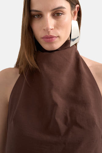 Bruine kleedje zonder mouwen van TOPSHOP met een hoge hals en een zilveren oorbel.