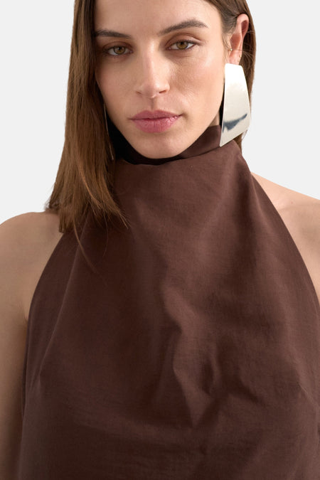 Bruine kleedje zonder mouwen van TOPSHOP met een hoge hals en een zilveren oorbel.