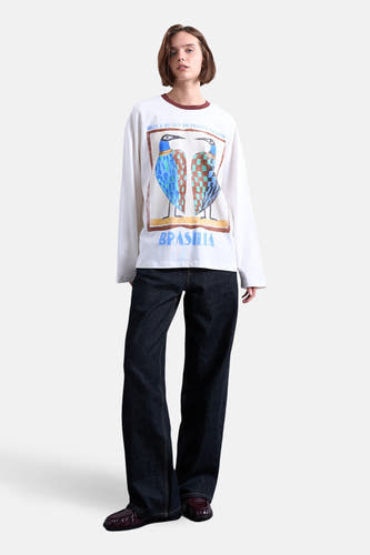T-shirt blanc à manches longues de TOPSHOP, avec imprimé d'oiseaux colorés et porté avec un jean foncé et des mocassins marron.
