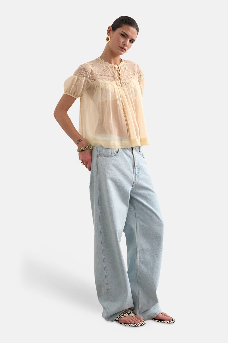 Blouse écru à manches courtes de TOPSHOP, avec détails en dentelle et devant drapé, associée à un jean ample et des sandales.