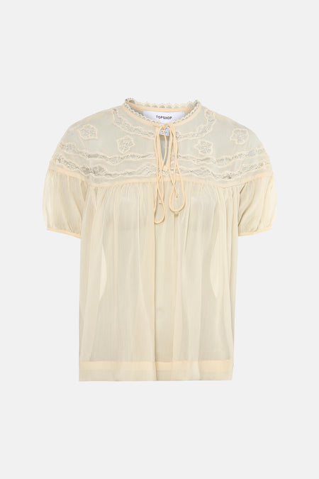 Blouse écru transparente à manches courtes de TOPSHOP, avec détails en dentelle et fermeture à nouer au col.
