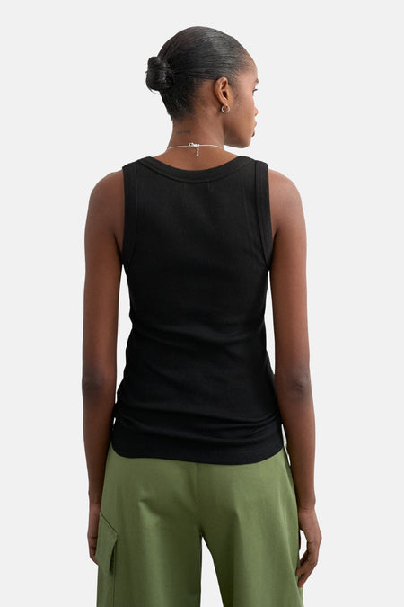 Débardeur noir de TOPSHOP, avec une texture côtelée et un col rond, porté avec un pantalon vert.