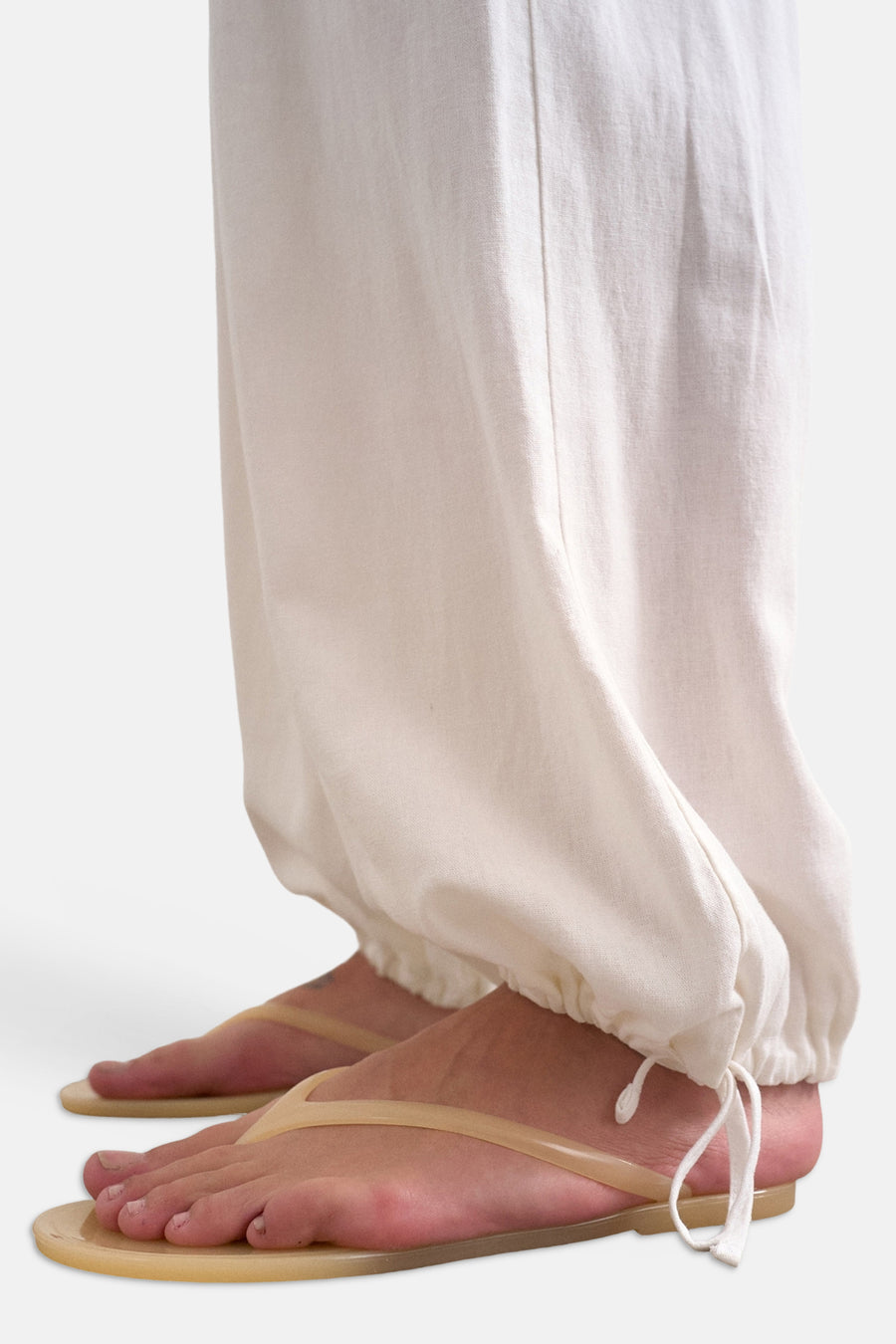Pantalon blanc de TOPSHOP avec cordon de serrage aux chevilles, porté avec des tongs jaunes.