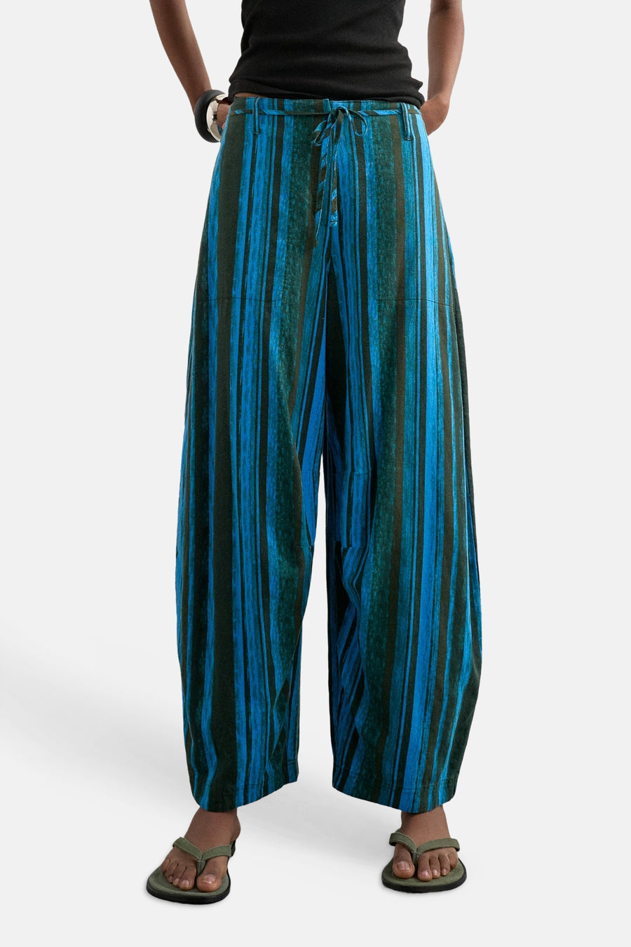Pantalon bleu de TOPSHOP, à rayures verticales bleues et vert foncé, avec cordon de serrage et jambes larges, porté avec un haut noir et des tongs.
