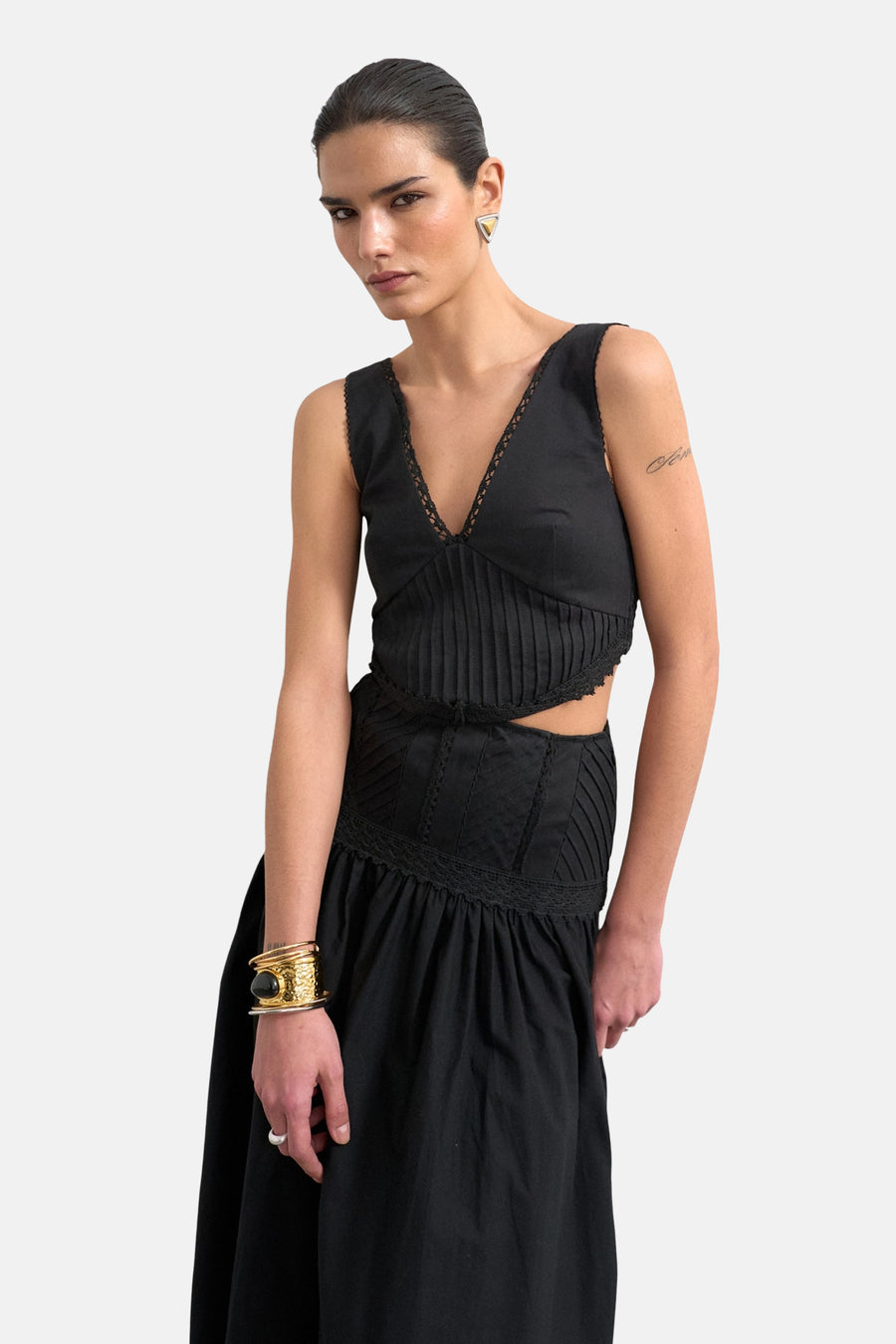 Zwart mouwloos kleedje van TOPSHOP met kanten V-hals en geplooide details, uitgesneden taille, gedragen door een model met gouden armband.