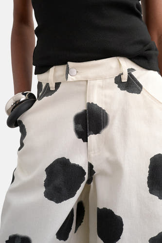 Pantalon écru de TOPSHOP, avec un motif à taches noires et un bracelet argenté au poignet.