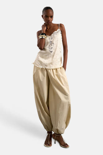 Blouse sans manches écru de TOPSHOP avec détails en dentelle, portée sur un pantalon large beige et des sandales à talons.