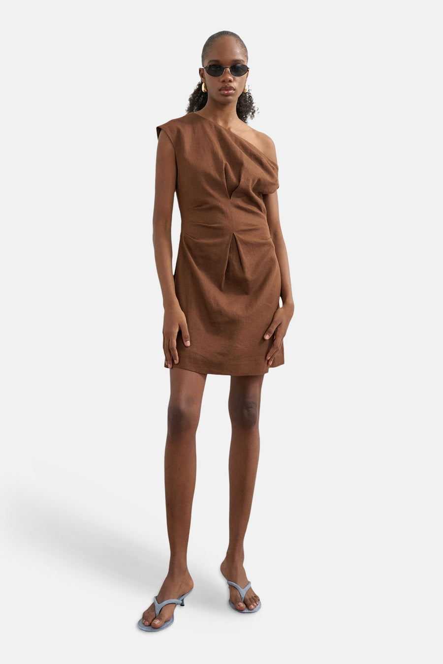 Mini-robe marron à une épaule de TOPSHOP avec devant drapé et plissé, porté par un mannequin avec des lunettes de soleil et des talons bleu clair.