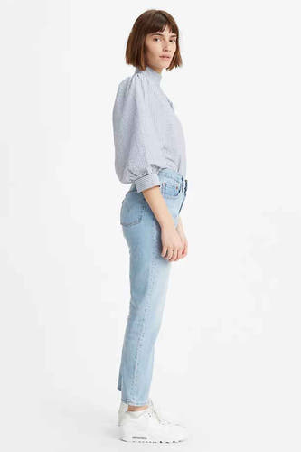 Femme en chemise rayée et jeans bleu clair, debout en profil.