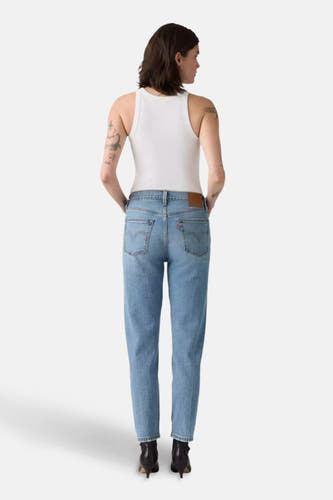 Lichtblauwe straight jeans van Levi's, met rode merklabel op de achterkant, gecombineerd met een witte tanktop en zwarte hakken.
