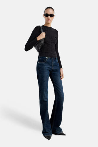 Zwarte ronde hals trui van MANGO, met ribstructuur, gedragen met donkerblauwe flared jeans en zwarte zonnebril, lifestyle shot.