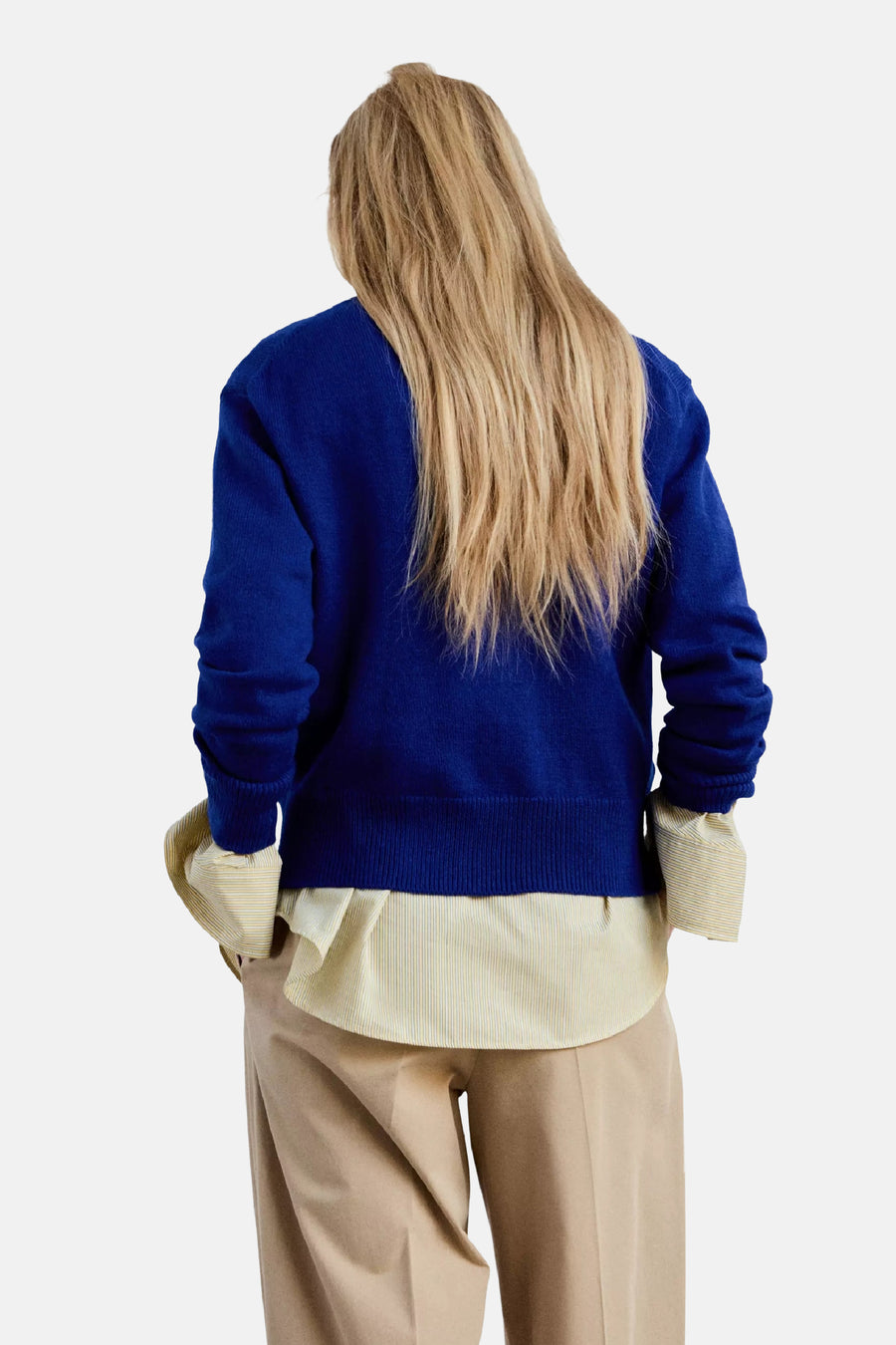 Blauwe V-hals trui van MANGO, achterzijde, met ribboorden en model in beige broek en gestreept overhemd