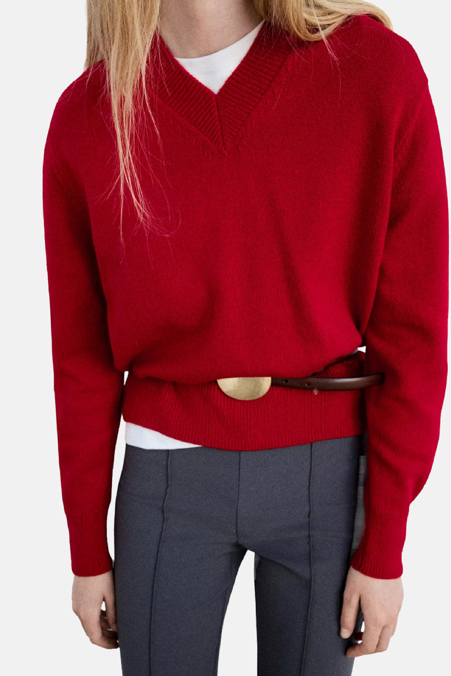 Rode V-hals trui van MANGO, gebreid met strakke ribboorden, gedragen over wit shirt en grijze broek, voorzien van bruine riem met gouden gesp, front view.