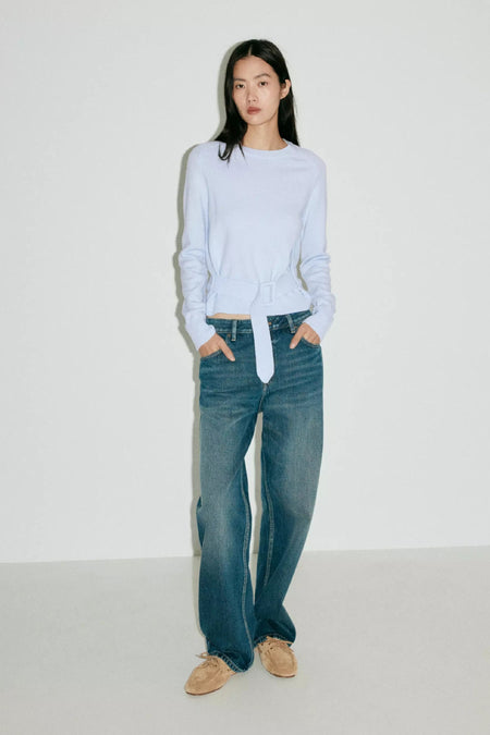 Lichtblauwe ronde hals trui van MANGO met riemdetail, gedragen met blauwe jeans en bruine schoenen, front view.