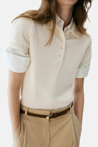 Ecru korte mouwen pull van MANGO met knoopsluiting, gebreide textuur en opgerolde mouwen, gedragen met beige broek en bruine riem