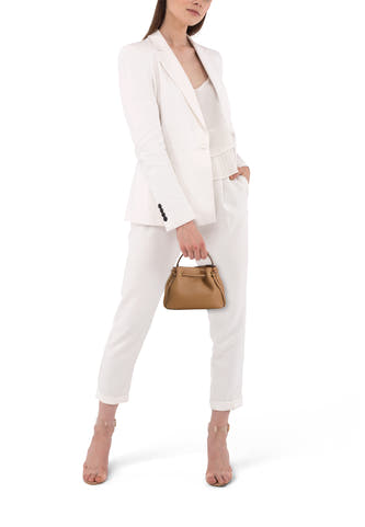 Bruine schoudertas van leer met goudkleurige sluiting, van MANGO, gedragen door model in witte jas en broek, lifestyle shot