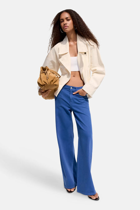 Blauwe damesbroek met wijde pijpen van MANGO, lichte denimstof, 5-pockets, lifestyle shot met wit topje en crèmekleurige jas