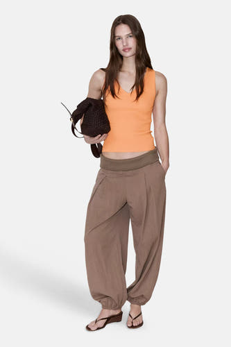 Oranje ribbeldebardeur van MANGO, strak model met V-hals, gedragen met bruine wijde broek en rieten tas, lifestyle shot