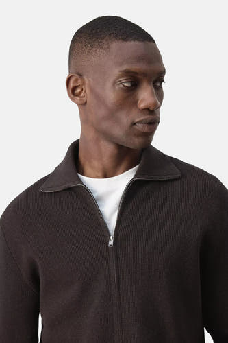 Bruine ribbelpull met rolkraag van MANGO, voorzien van rits en gedragen over een wit T-shirt, close-up vooraanzicht