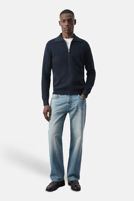 Blauwe gebreide gilet met rolkraag en rits van MANGO, gedragen met witte t-shirt, lichtblauwe jeans en zwarte loafers, front view.