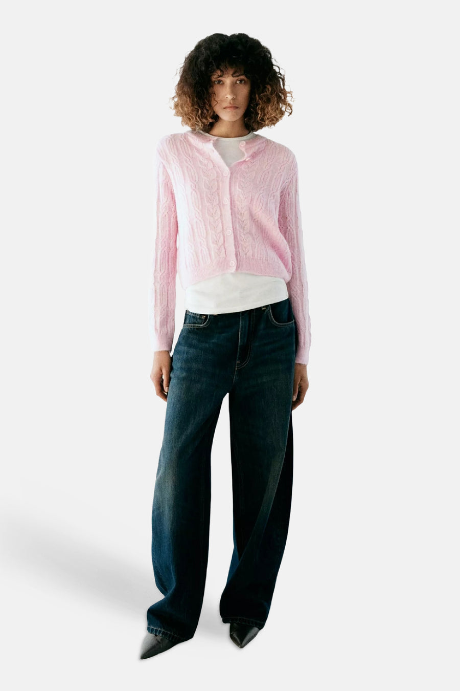 Roze gebreide gilet met kabelpatroon van MANGO, gedragen over witte top en donkerblauwe wijde jeans, front view
