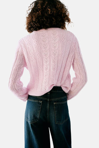 Roze gebreide gilet van MANGO, met kabelpatroon en open rug, achterzijde weergegeven op model in donkerblauwe jeans